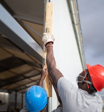 Two Afro-American builders wearing helmets and face masks while measuring the wall